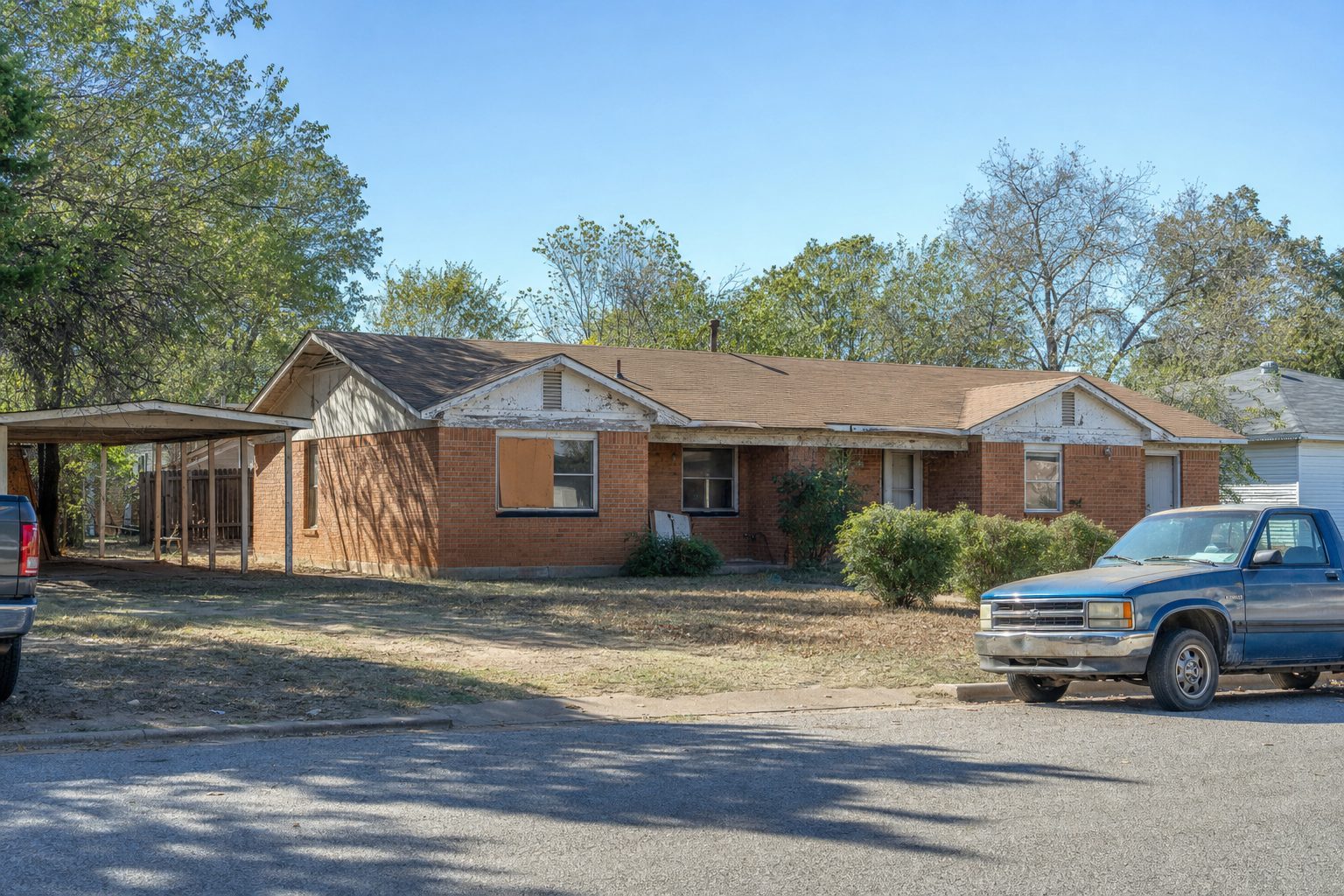 A duplex-style brick rental property in a Fort Worth neighborhood with weathered trim, mature trees, and street parking — a tired landlord property