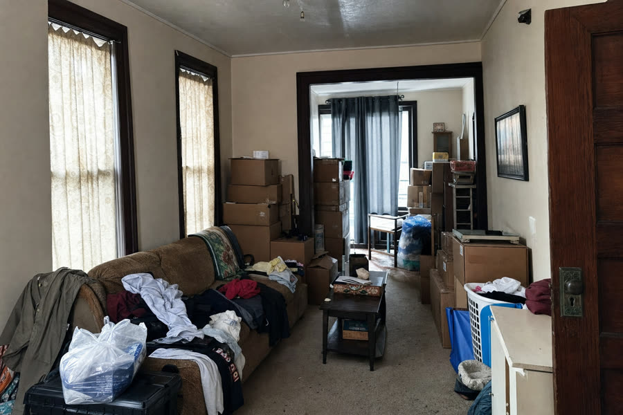 Cluttered living room with stacked boxes and piles of belongings